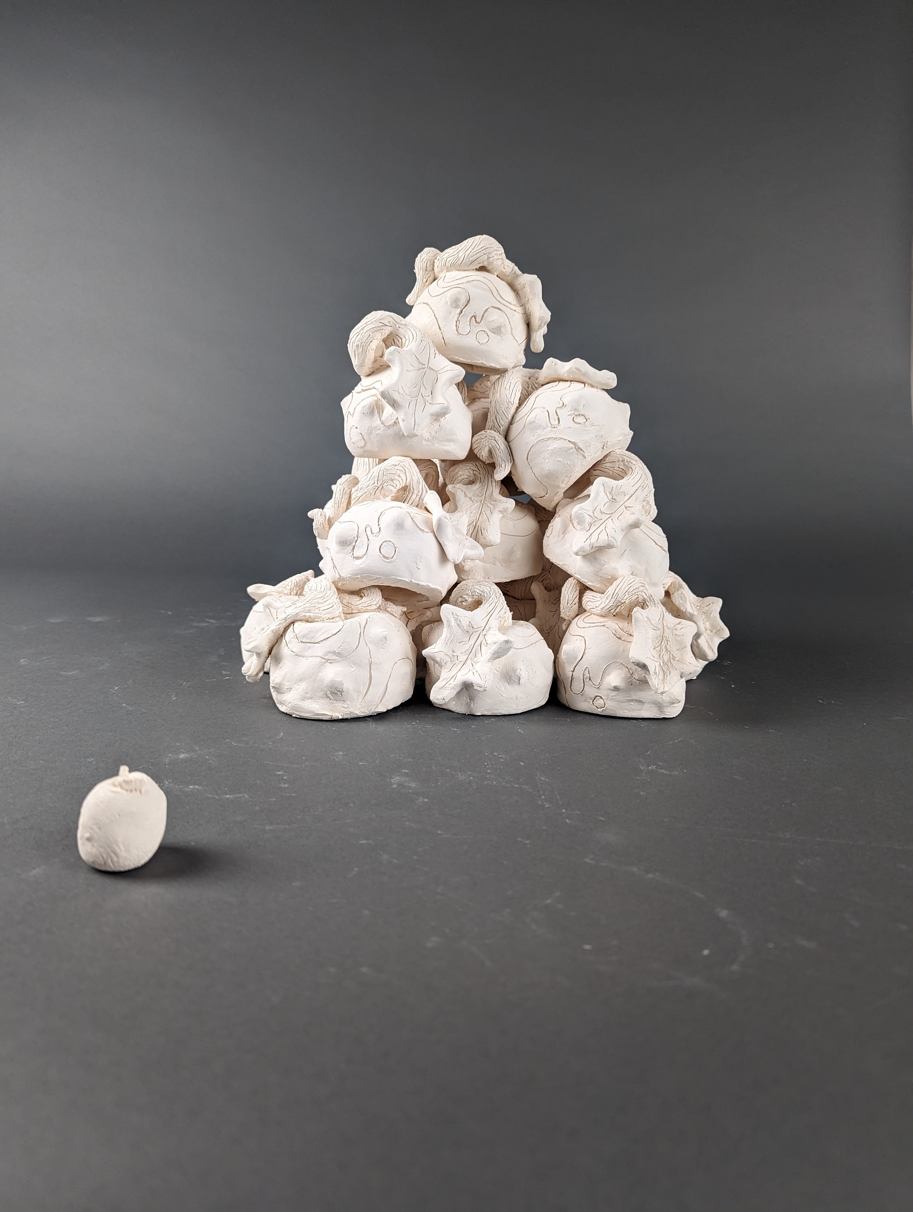 A tower of apples on a grey background made from clay and unglazed.