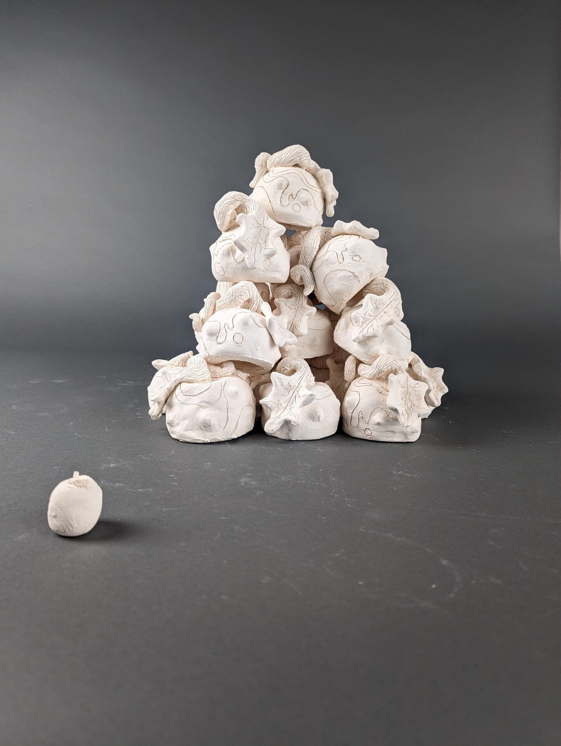 A tower of apples on a grey background made from clay and unglazed.