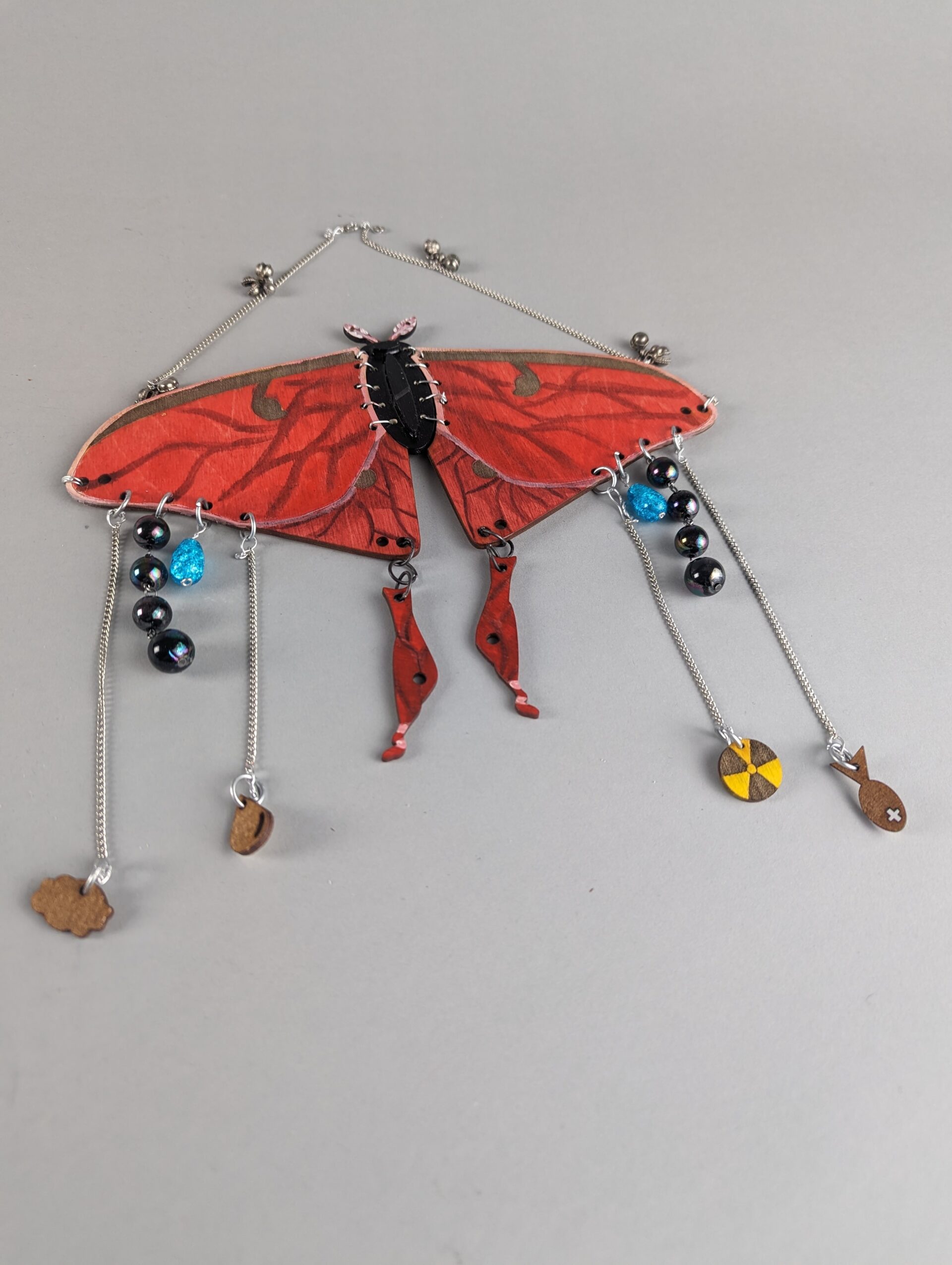 Depicting a phisical art peaice  of a red Luna moth dripping with pollution imagery. meant to be worn as a mask.